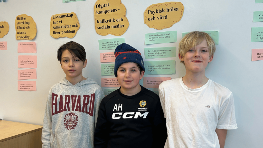 Tre pojkar i årskurs fem står mot en vägg och ler mot kameran.